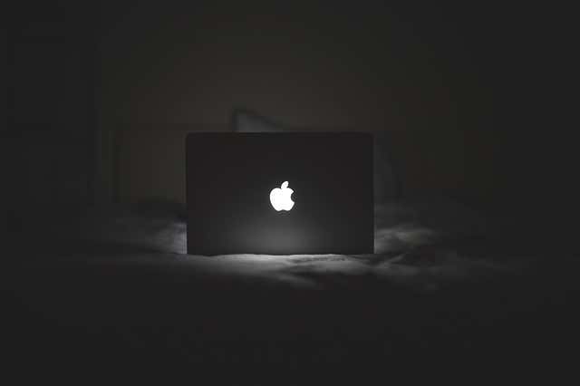 MacBook on a bed in a dark room with the Apple logo lit